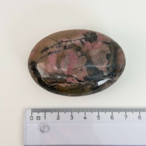 Rhodonit håndsten krystal sten ved siden af lineal på hvid baggrund