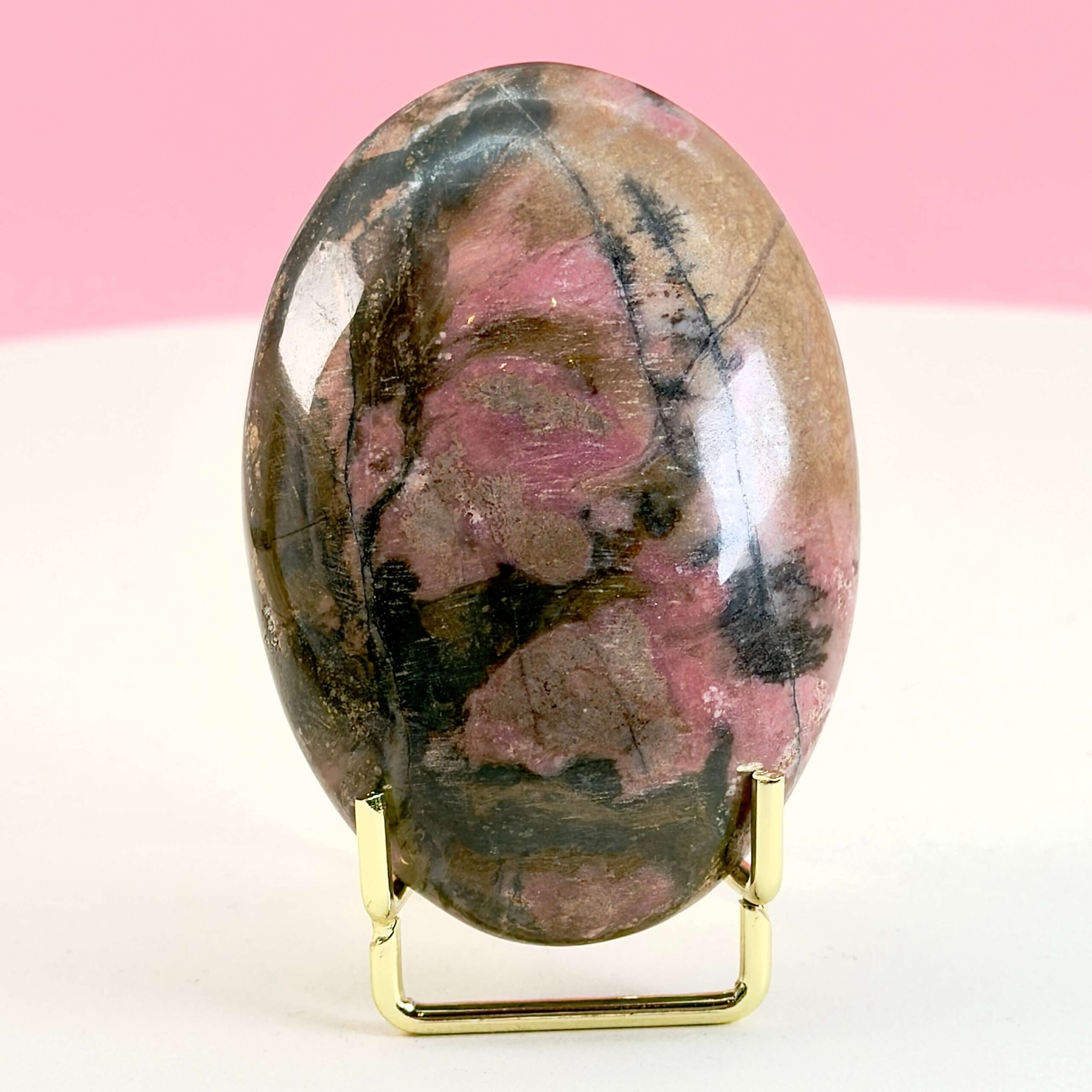 Rhodonit håndsten krystal sten i holder på hvid plade med lyserød baggrund