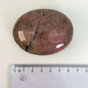 Rhodonit håndsten krystal sten ved siden af lineal på hvid baggrund