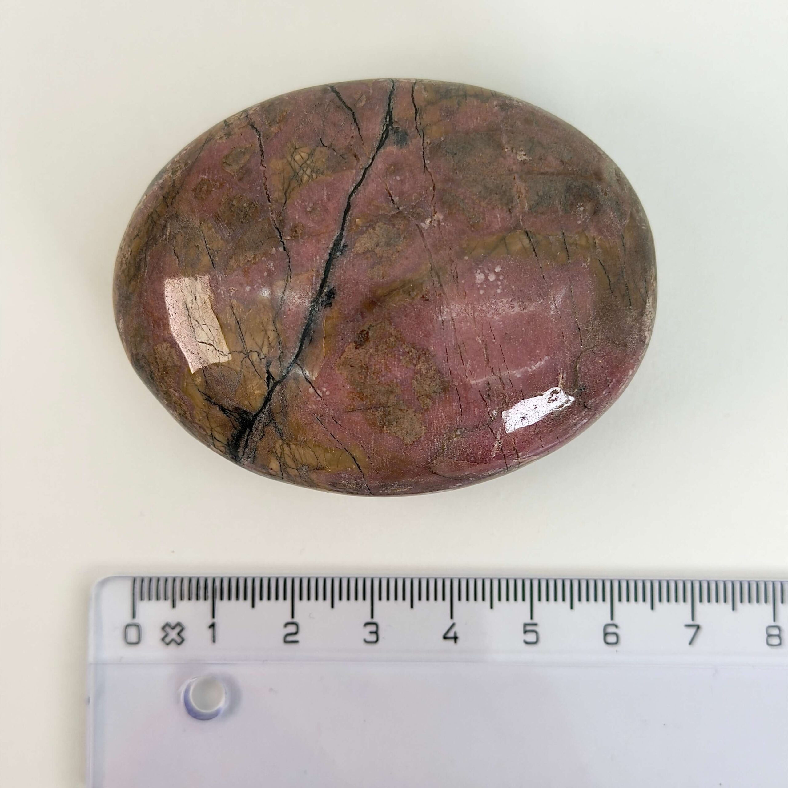 Rhodonit håndsten krystal sten ved siden af lineal på hvid baggrund