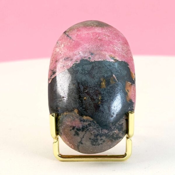 Rhodonit håndsten krystal sten i holder på hvid plade med lyserød baggrund