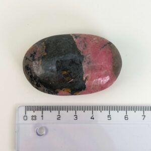 Rhodonit håndsten krystal sten ved siden af lineal på hvid baggrund