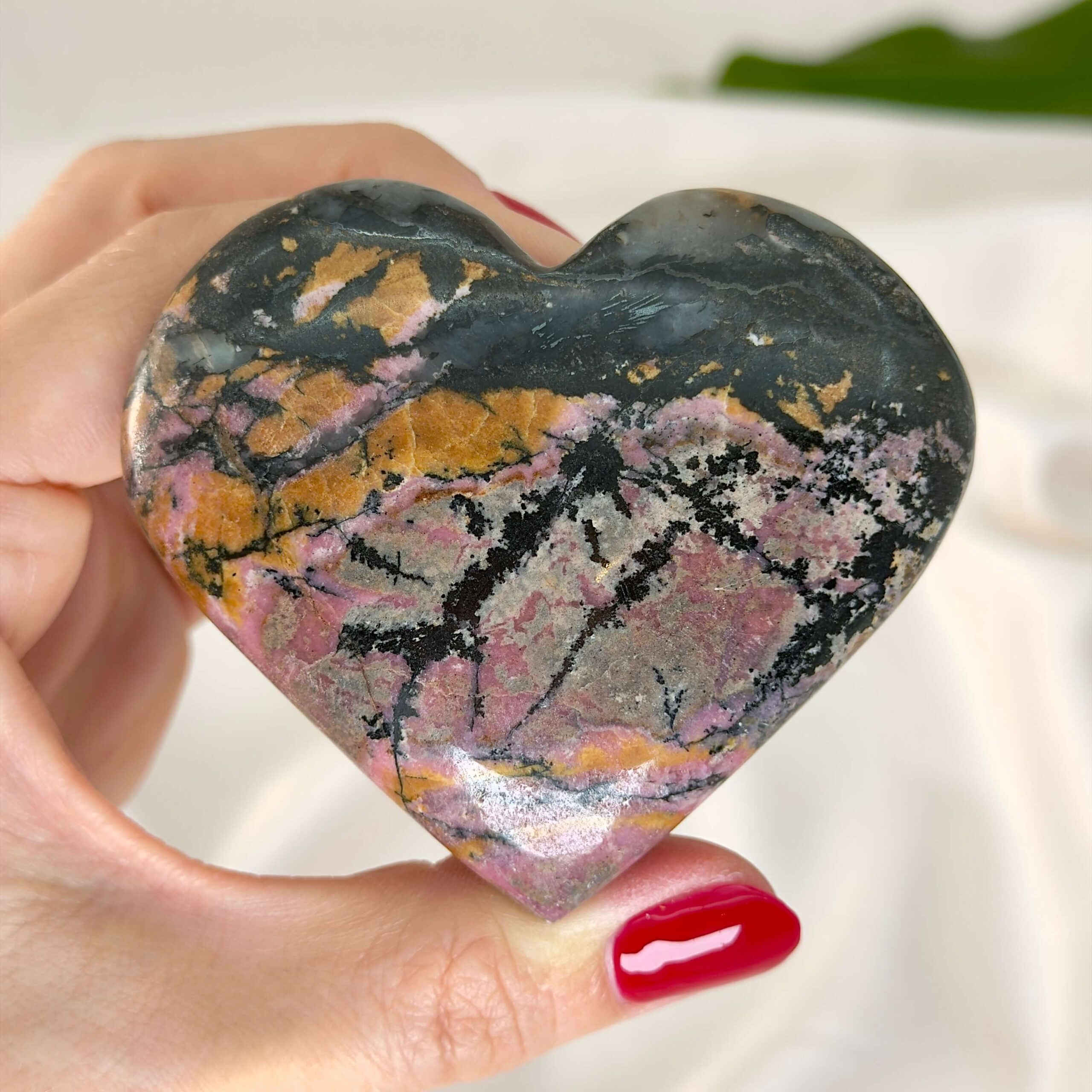 Rhodonit hjerte krystal sten i hånd med hvid baggrund