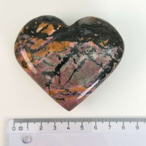 Rhodonit hjerte krystal sten ved siden af lineal på hvid baggrund