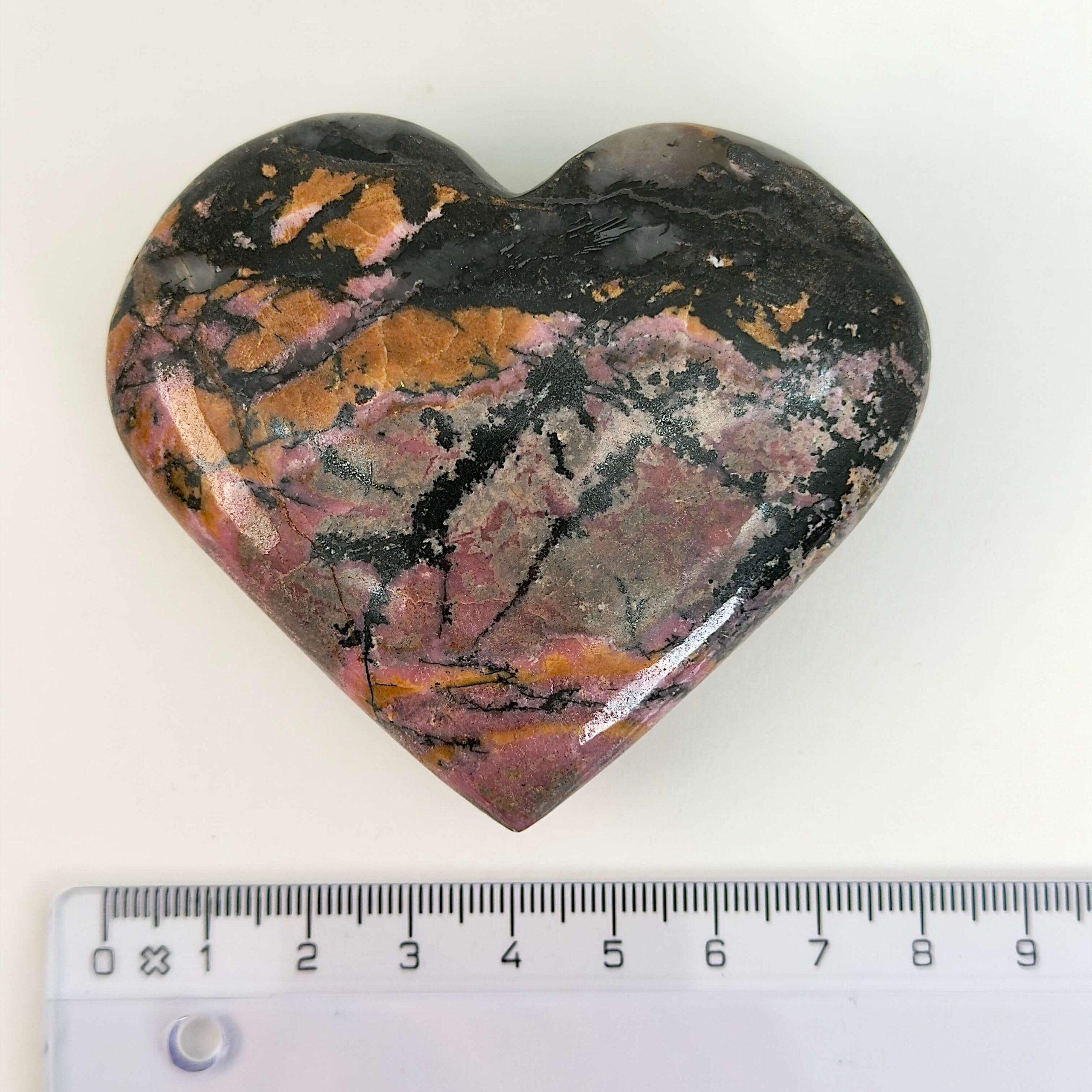 Rhodonit hjerte krystal sten ved siden af lineal på hvid baggrund