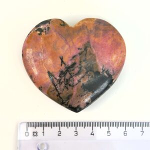 Rhodonit hjerte krystal sten ved siden af lineal på hvid baggrund