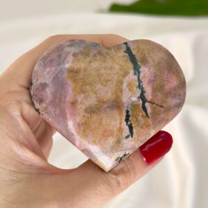 Rhodonit hjerte krystal sten i hånd med hvid baggrund