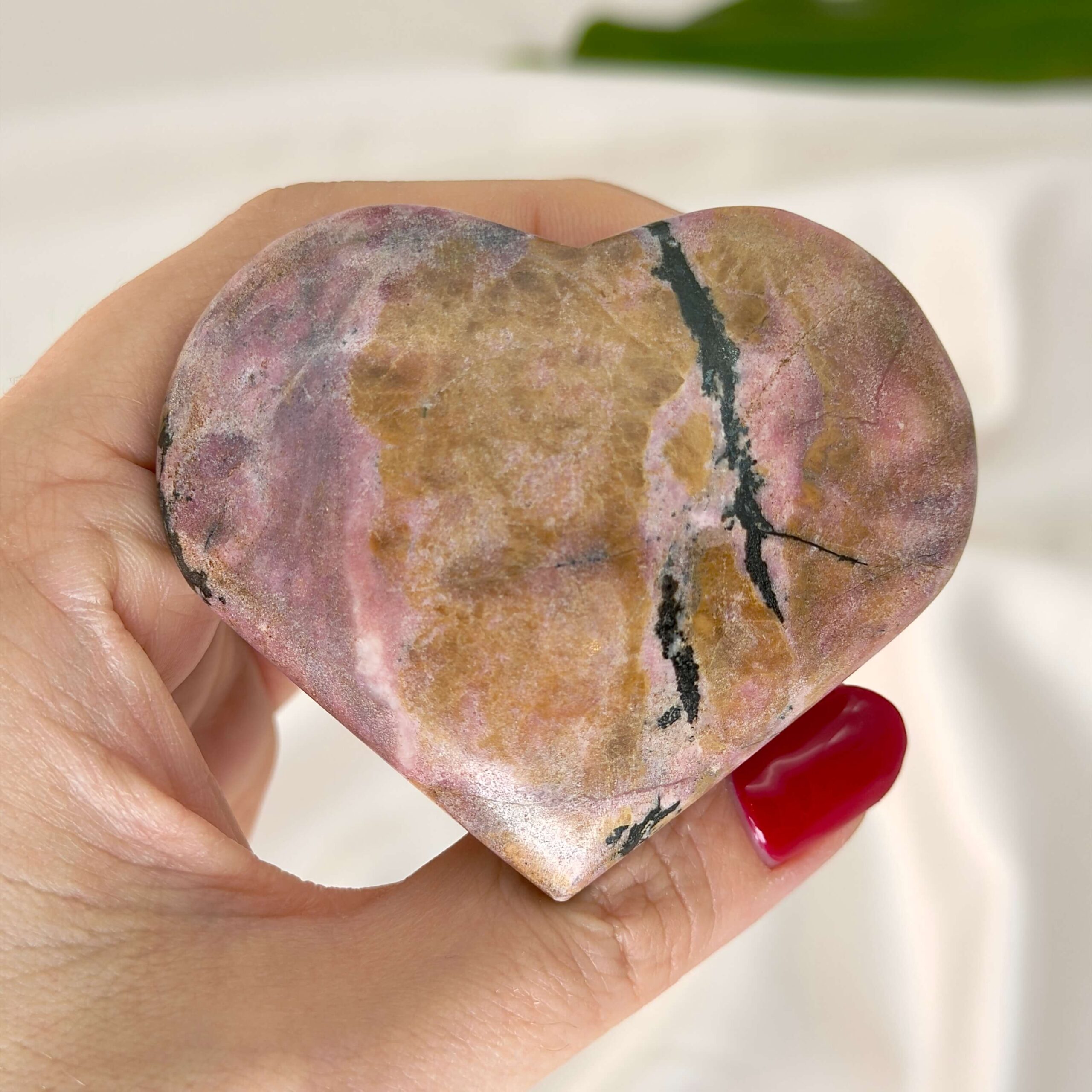 Rhodonit hjerte krystal sten i hånd med hvid baggrund