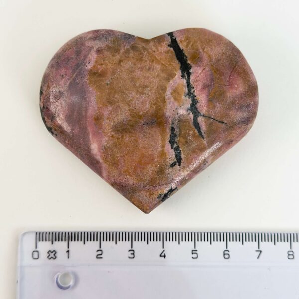 Rhodonit hjerte krystal sten ved siden af lineal på hvid baggrund