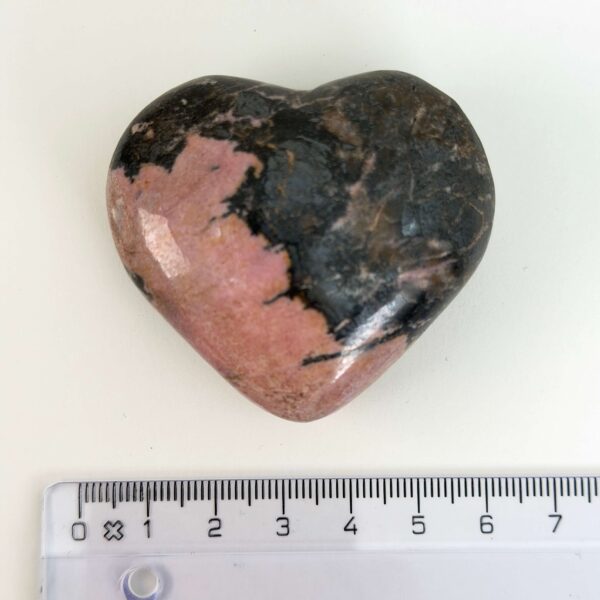 Rhodonit hjerte krystal sten ved siden af lineal på hvid baggrund