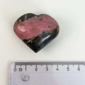 Rhodonit hjerte krystal sten ved siden af lineal på hvid baggrund