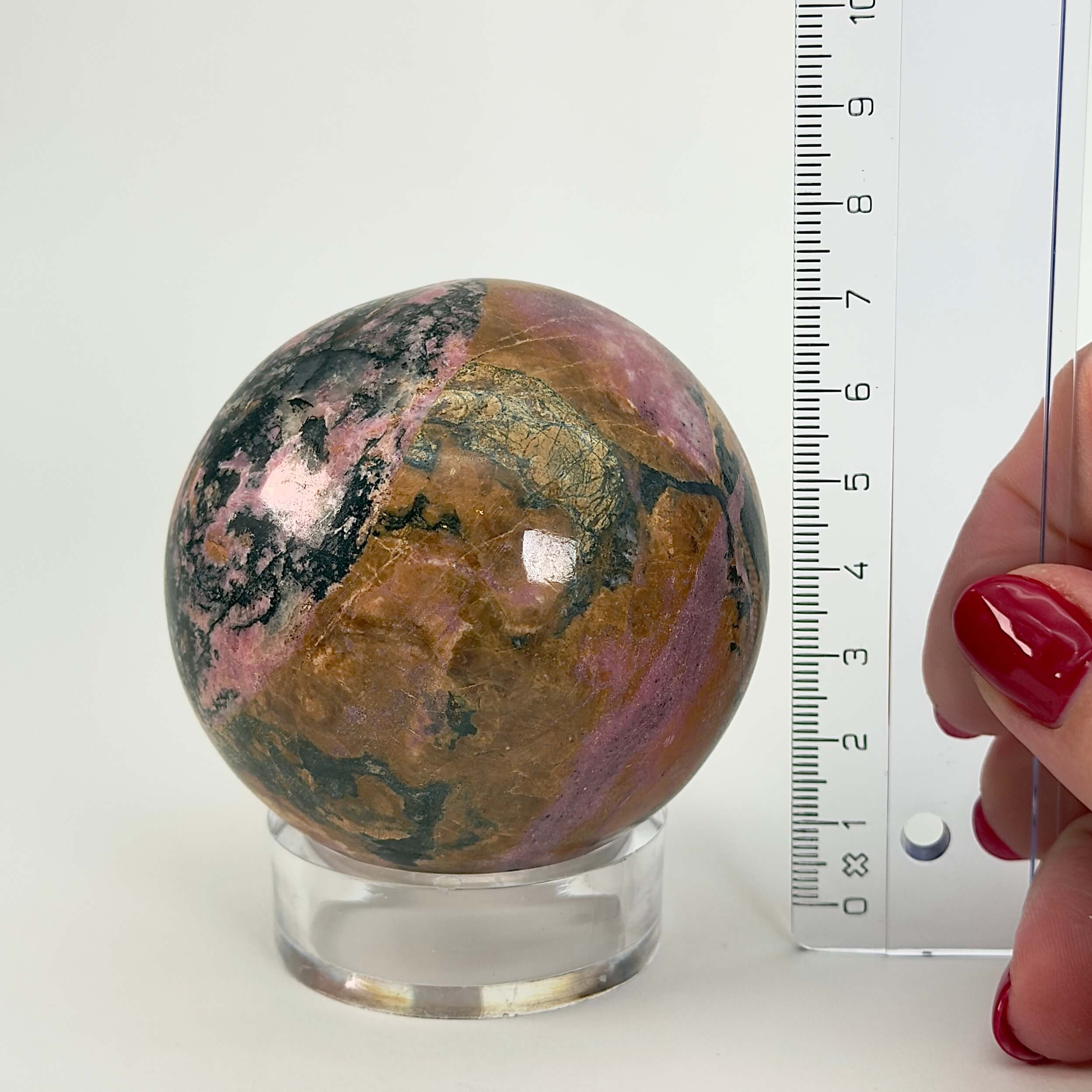 Rhodonit kugle krystal sten ved siden af lineal på hvid baggrund