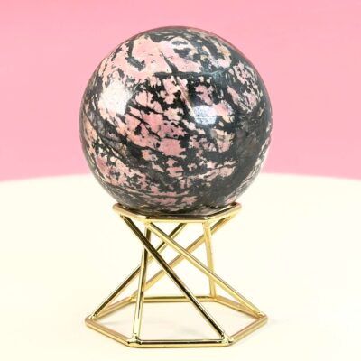 Rhodonit kugle krystal sten på stander på hvid plade med lyserød baggrund