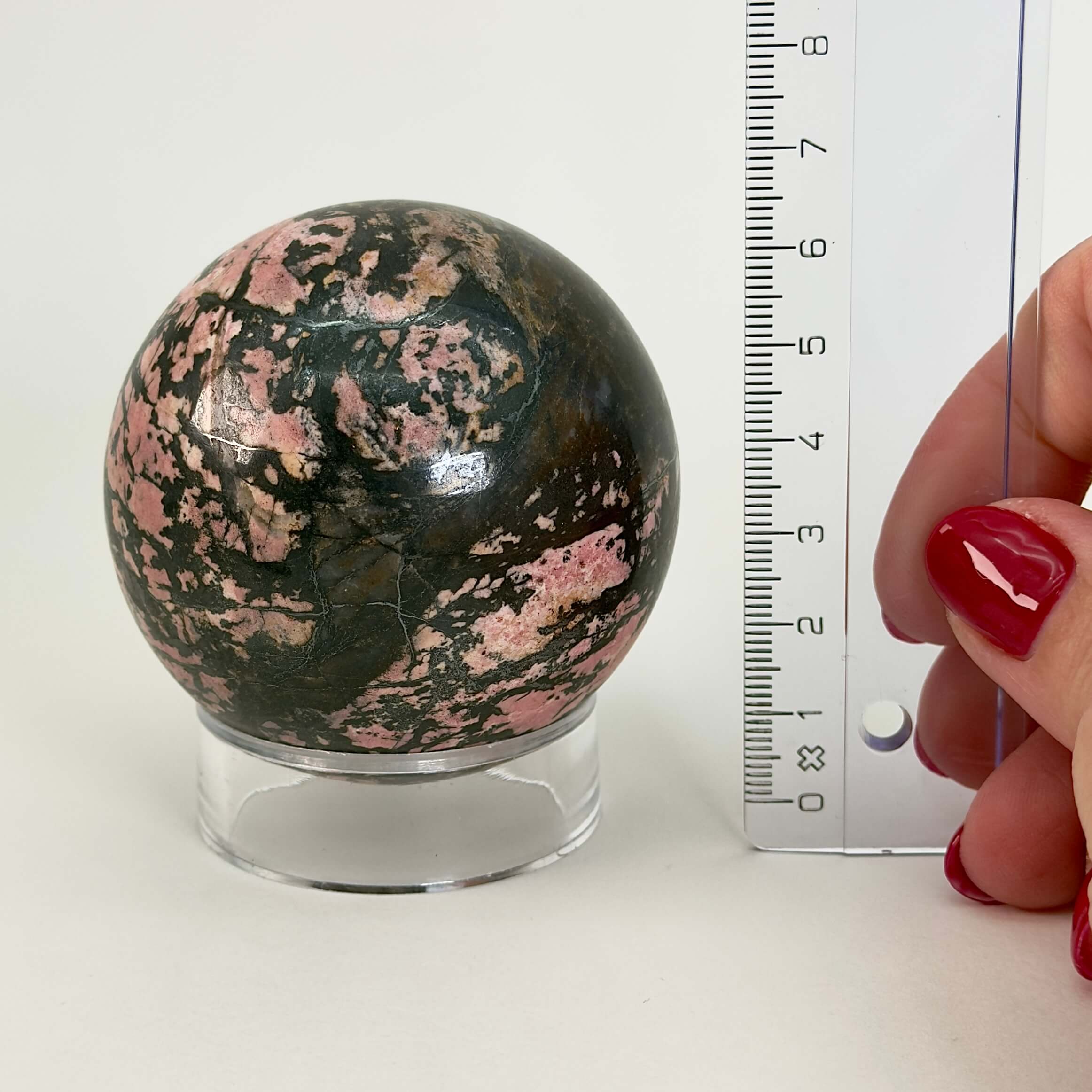 Rhodonit kugle krystal sten ved siden af lineal på hvid baggrund