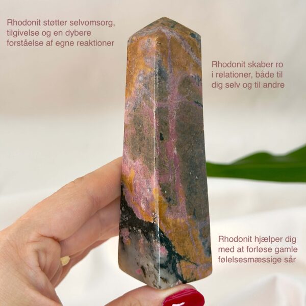 Rhodonit tårn krystal sten i hånd med hvid baggrund og med tags