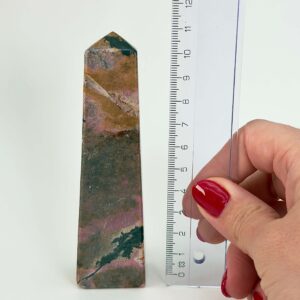 Rhodonit tårn krystal sten ved siden af lineal på hvid baggrund