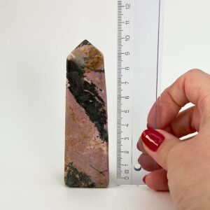 Rhodonit tårn krystal sten ved siden af lineal på hvid baggrund