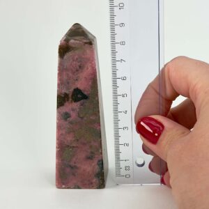 Rhodonit tårn krystal sten ved siden af lineal på hvid baggrund