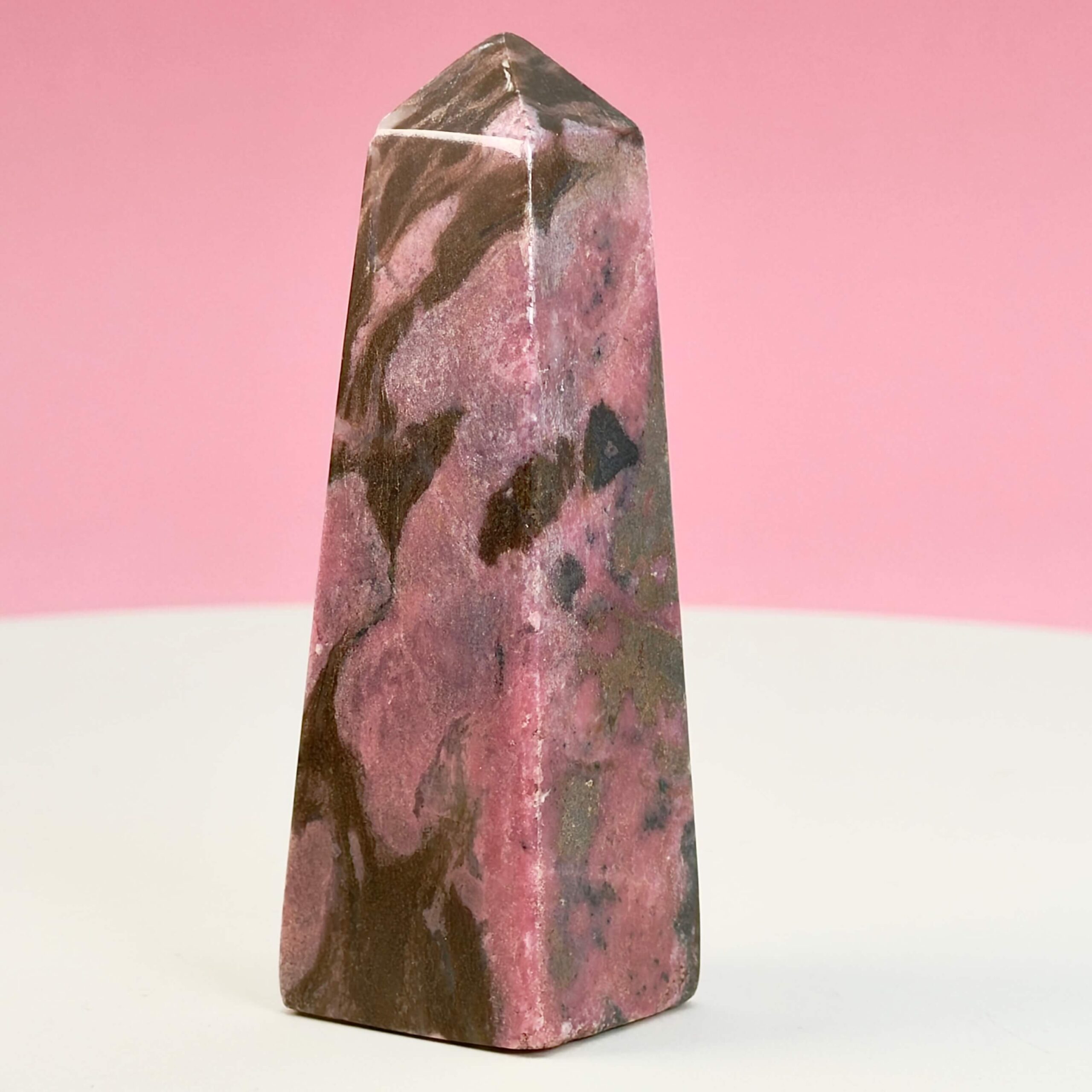 Rhodonit tårn krystal sten på hvid plade med lyserød baggrund