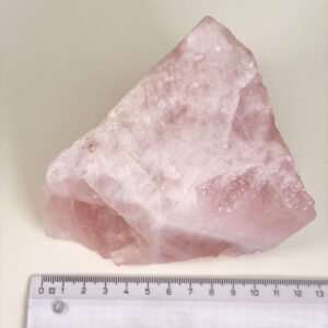 Rosakvarts Rå krystal sten med lineal på hvid baggrund