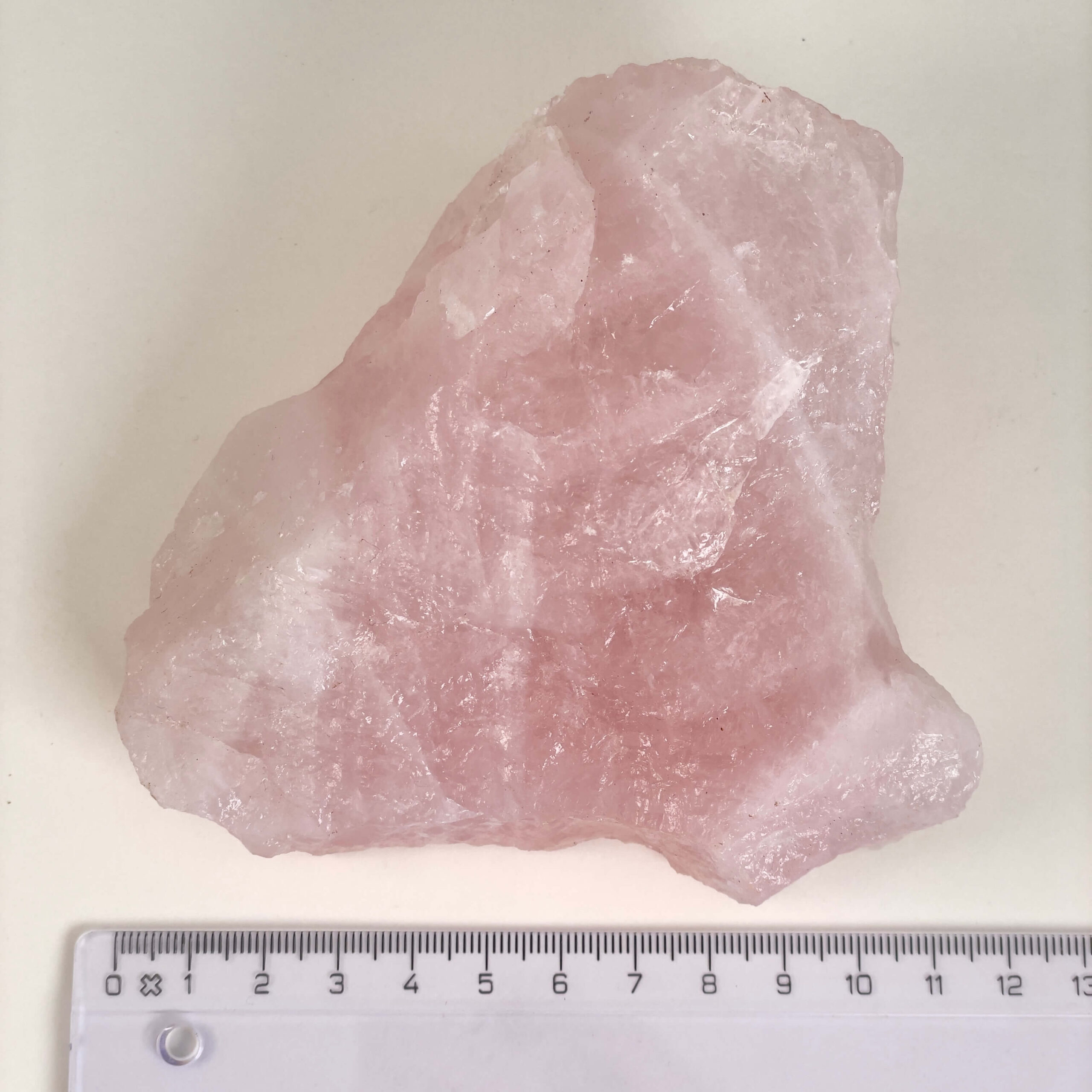 Rosakvarts Rå krystal sten med lineal på hvid baggrund
