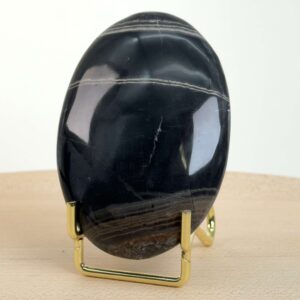 Sort Båndet Onyx Håndsten med glat, poleret overflade og naturlige sorte, grå og hvide bånd, der symboliserer grounding, beskyttelse og indre styrke.