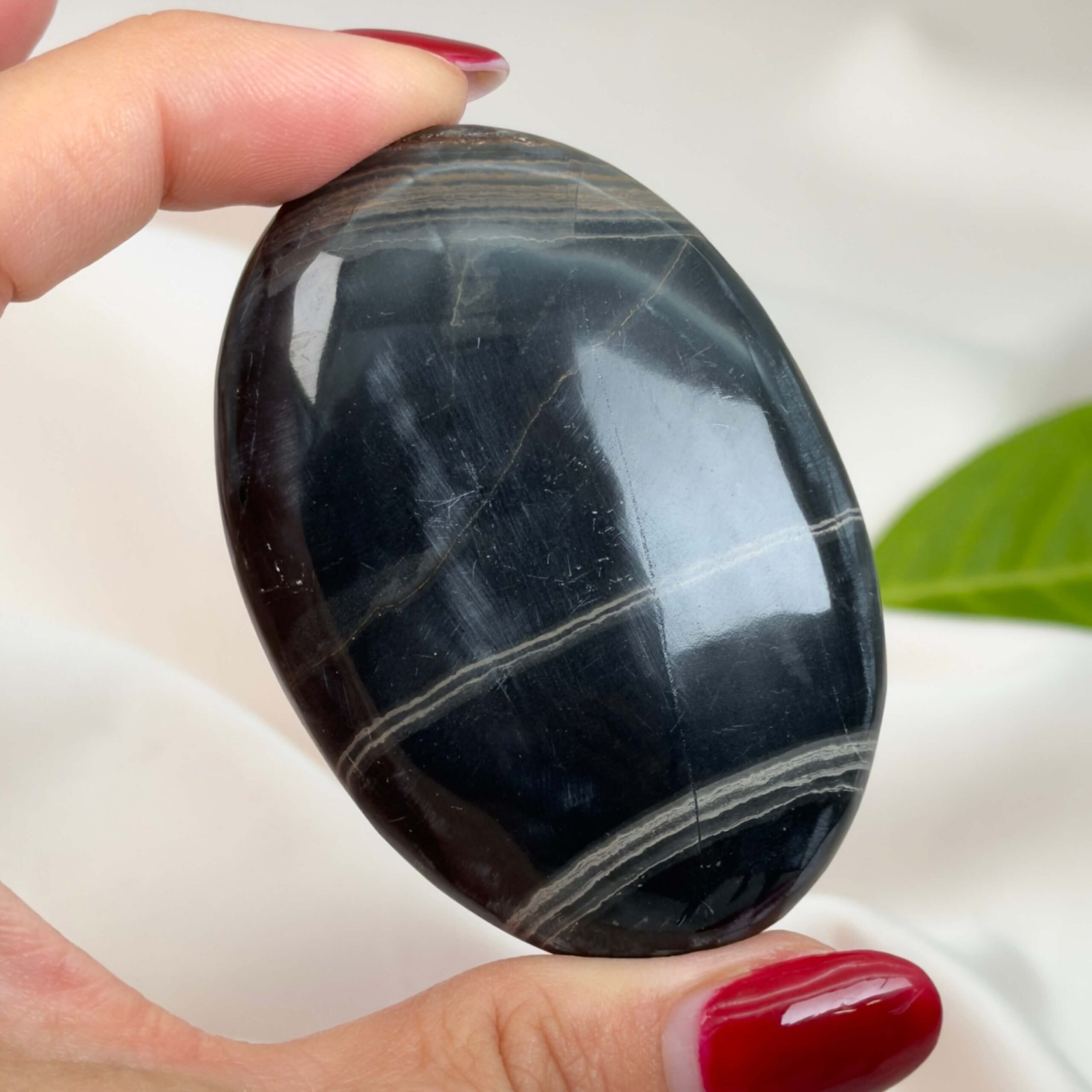 Sort Båndet Onyx Håndsten med glat, poleret overflade og naturlige sorte, grå og hvide bånd, der symboliserer grounding, beskyttelse og indre styrke.