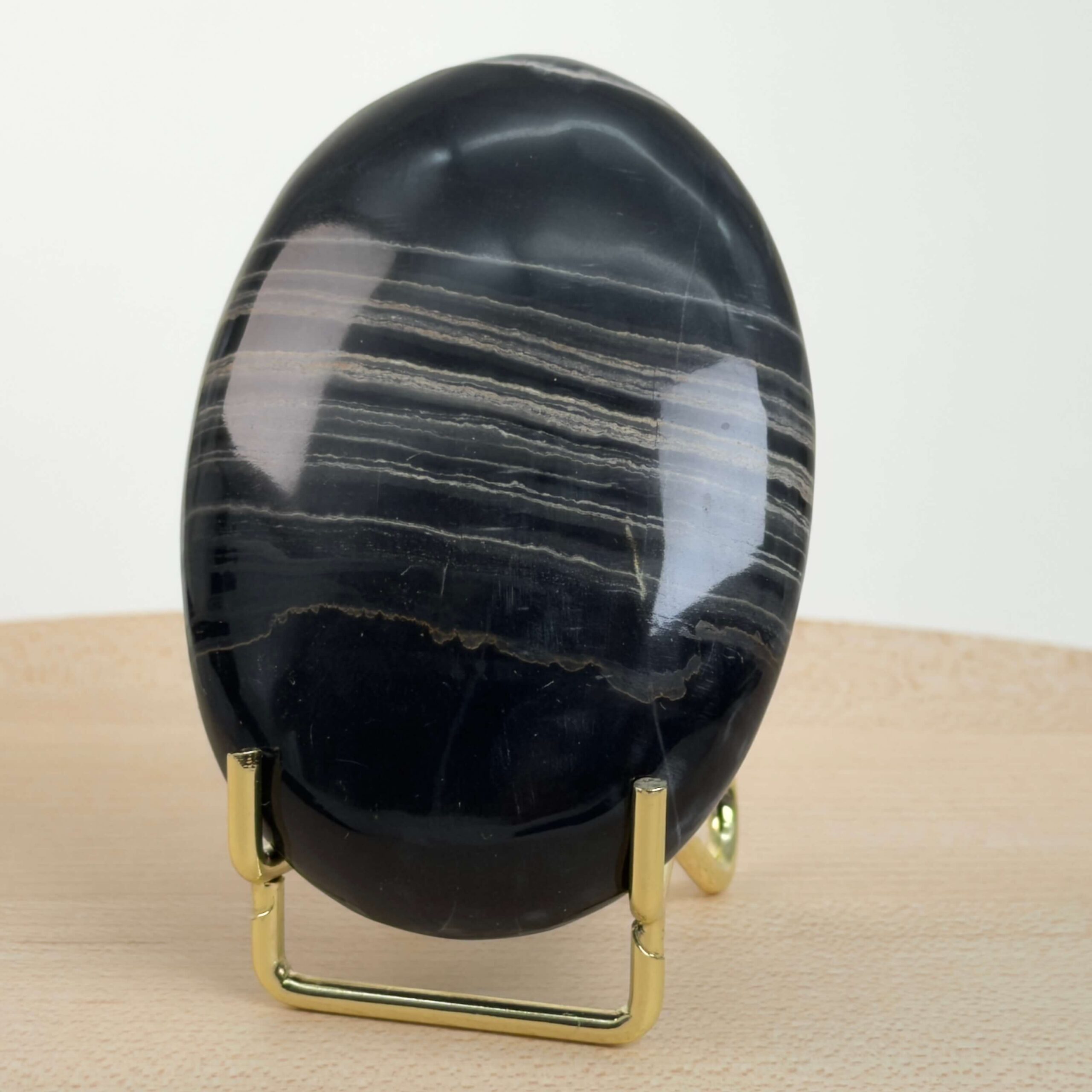 Sort Båndet Onyx Håndsten med glat, poleret overflade og naturlige sorte, grå og hvide bånd, der symboliserer grounding, beskyttelse og indre styrke.