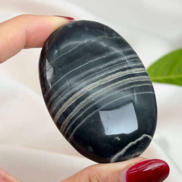 Sort Båndet Onyx Håndsten med glat, poleret overflade og naturlige sorte, grå og hvide bånd, der symboliserer grounding, beskyttelse og indre styrke.