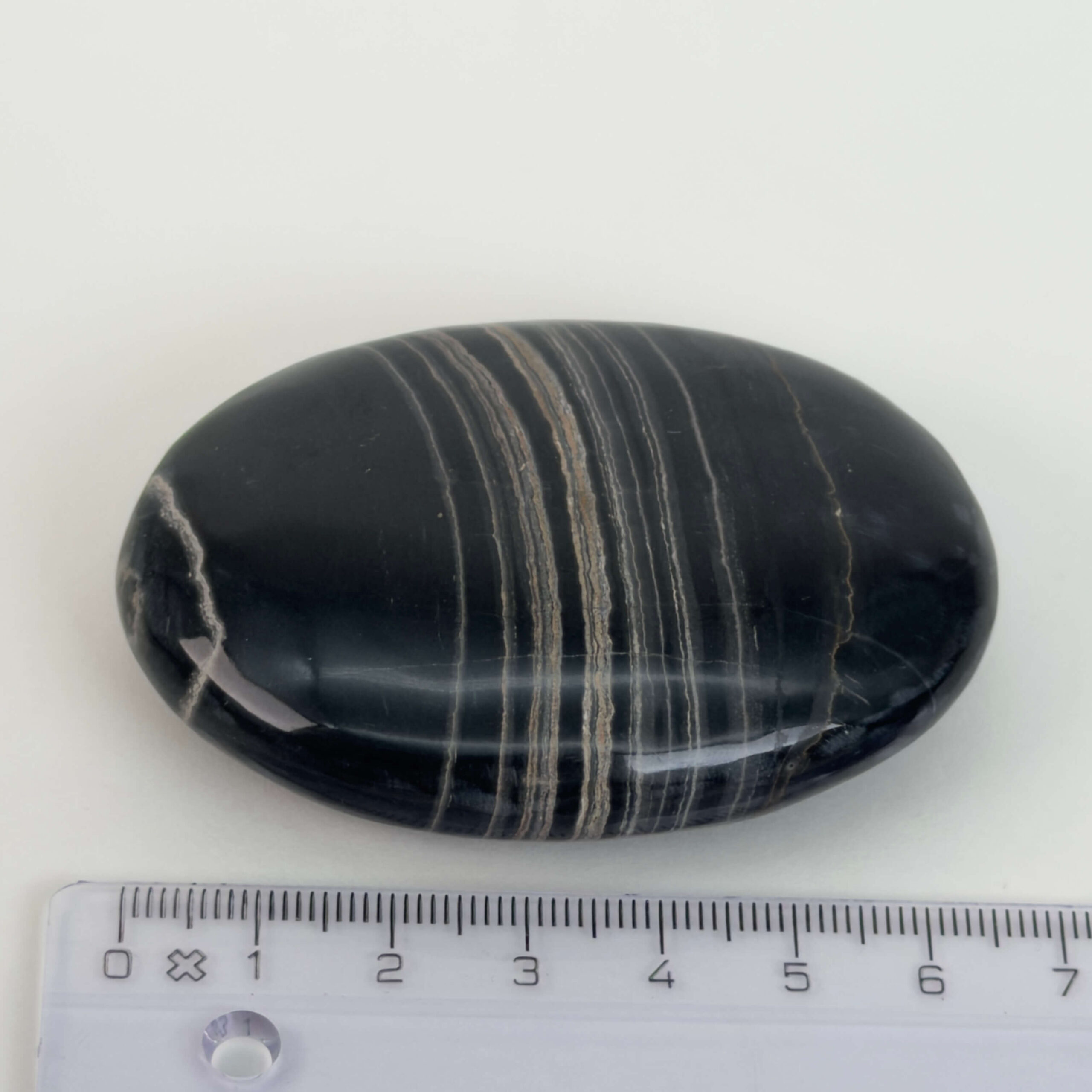 Sort Båndet Onyx Håndsten med glat, poleret overflade og naturlige sorte, grå og hvide bånd, der symboliserer grounding, beskyttelse og indre styrke.