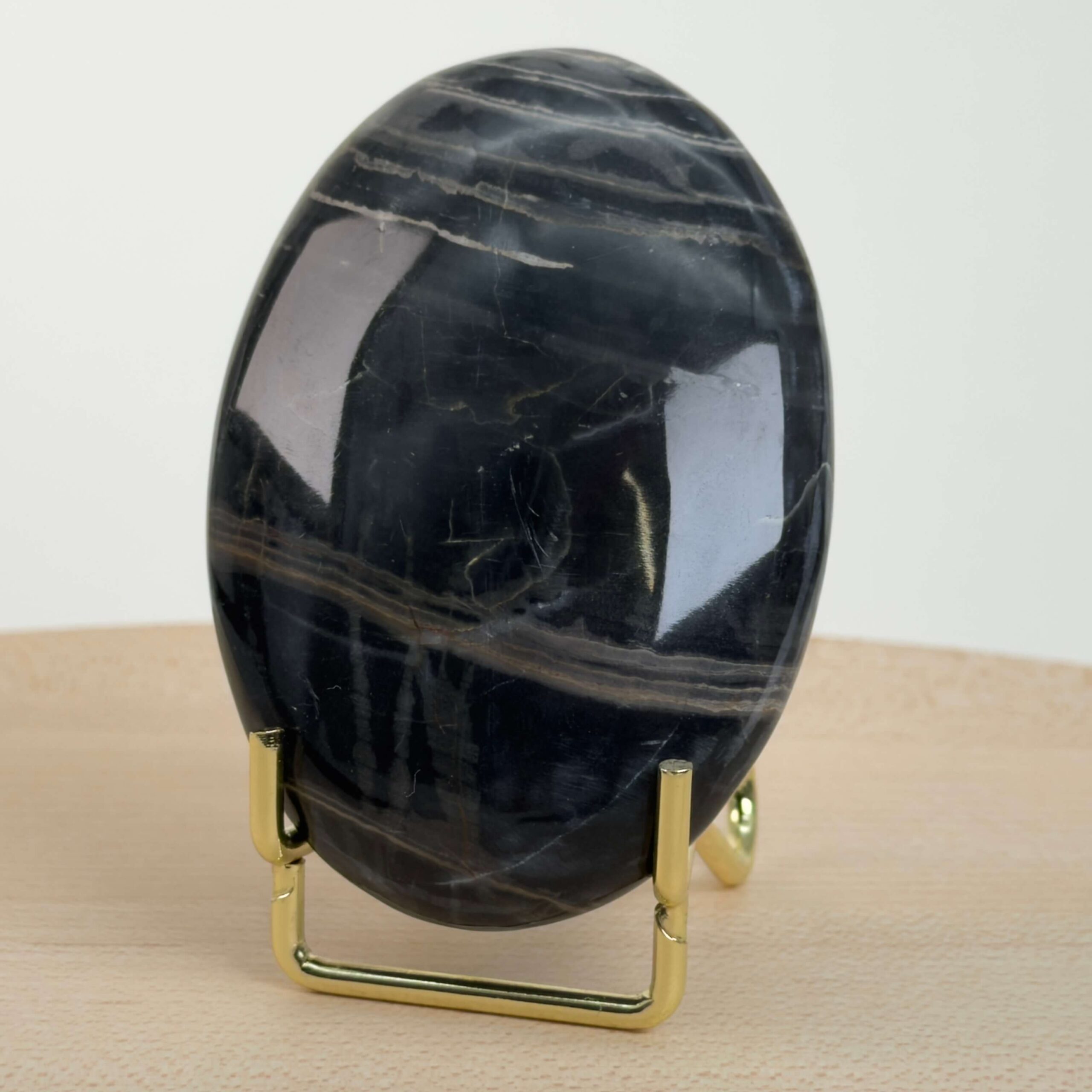 Sort Båndet Onyx Håndsten med glat, poleret overflade og naturlige sorte, grå og hvide bånd, der symboliserer grounding, beskyttelse og indre styrke.