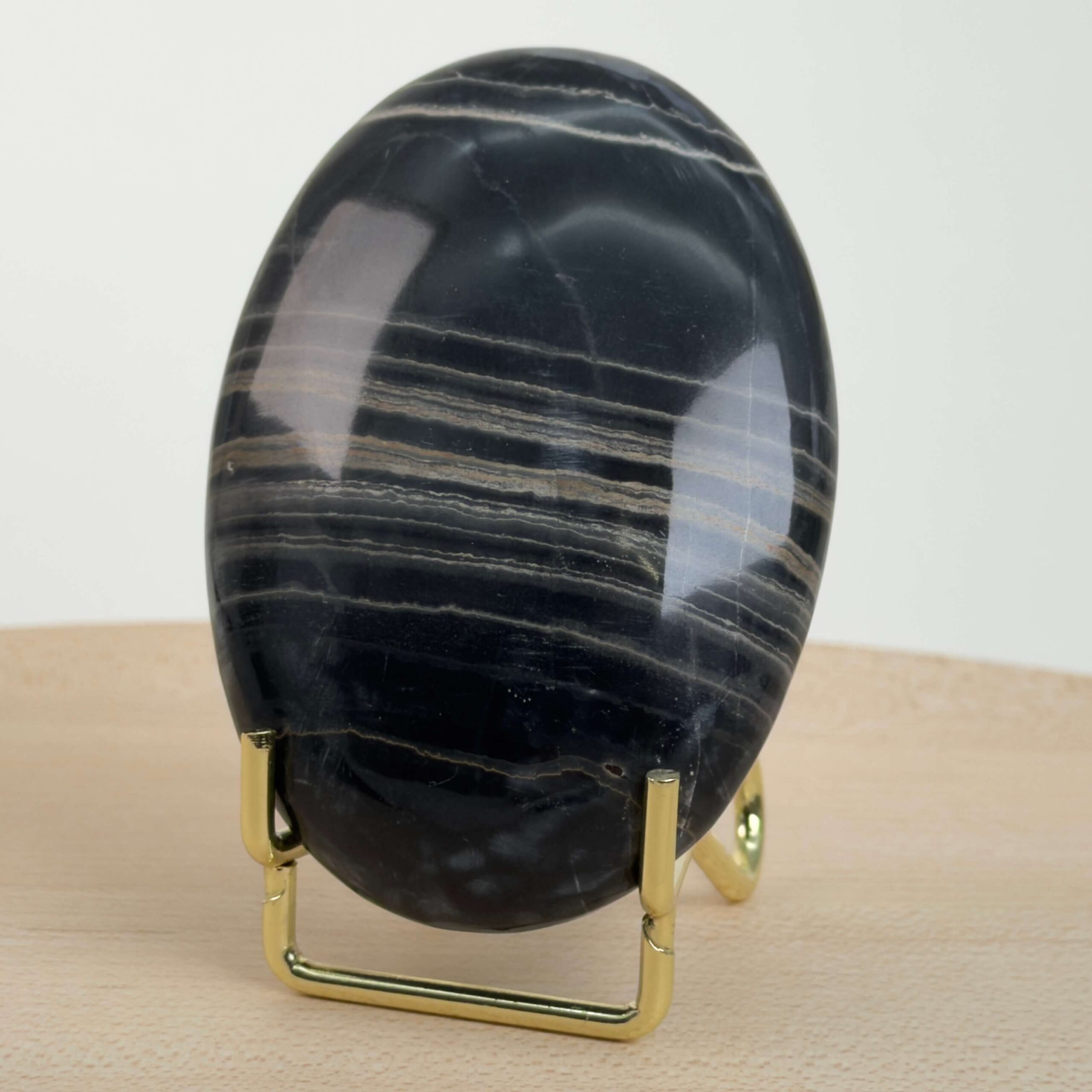 Sort Båndet Onyx Håndsten med glat, poleret overflade og naturlige sorte, grå og hvide bånd, der symboliserer grounding, beskyttelse og indre styrke.