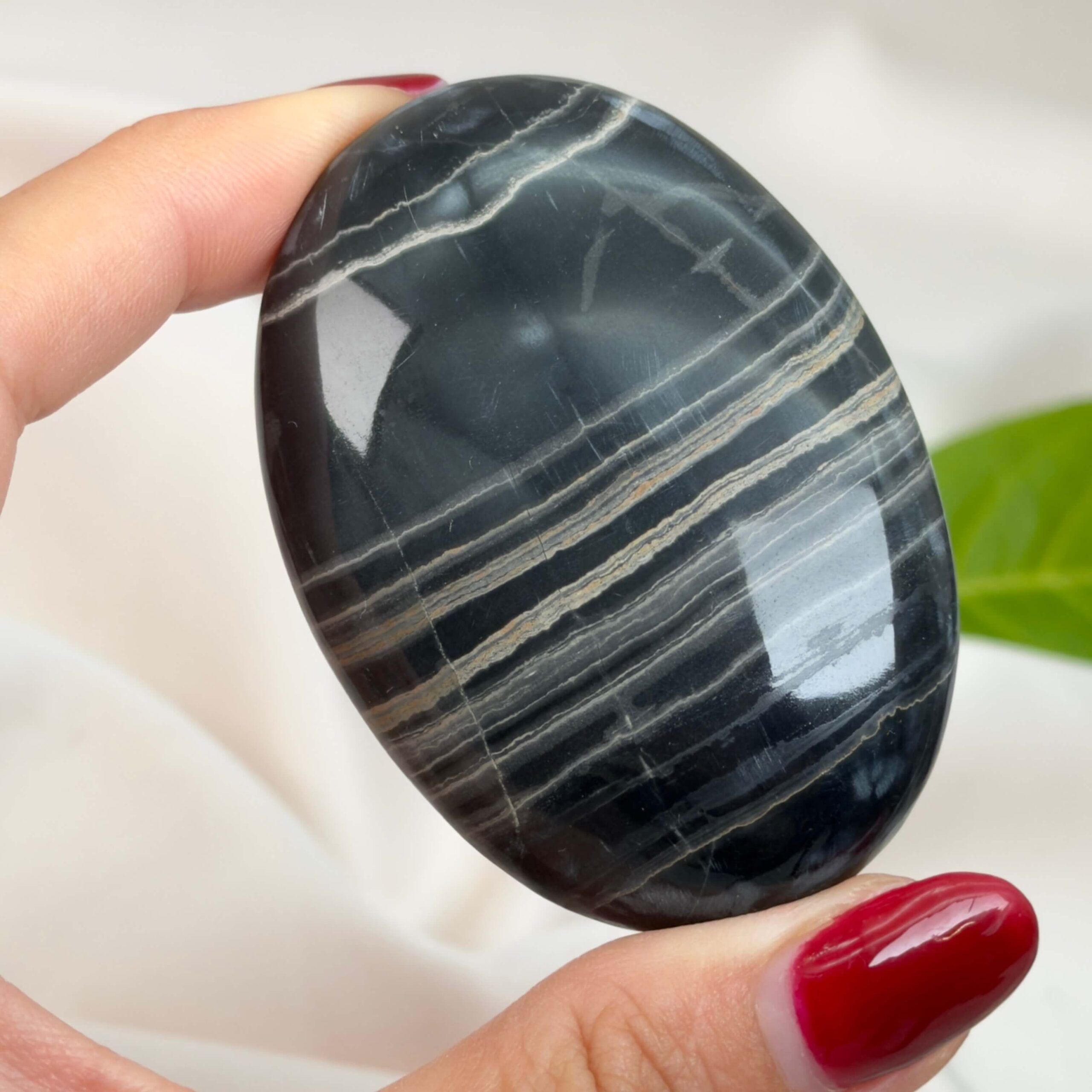 Sort Båndet Onyx Håndsten med glat, poleret overflade og naturlige sorte, grå og hvide bånd, der symboliserer grounding, beskyttelse og indre styrke.