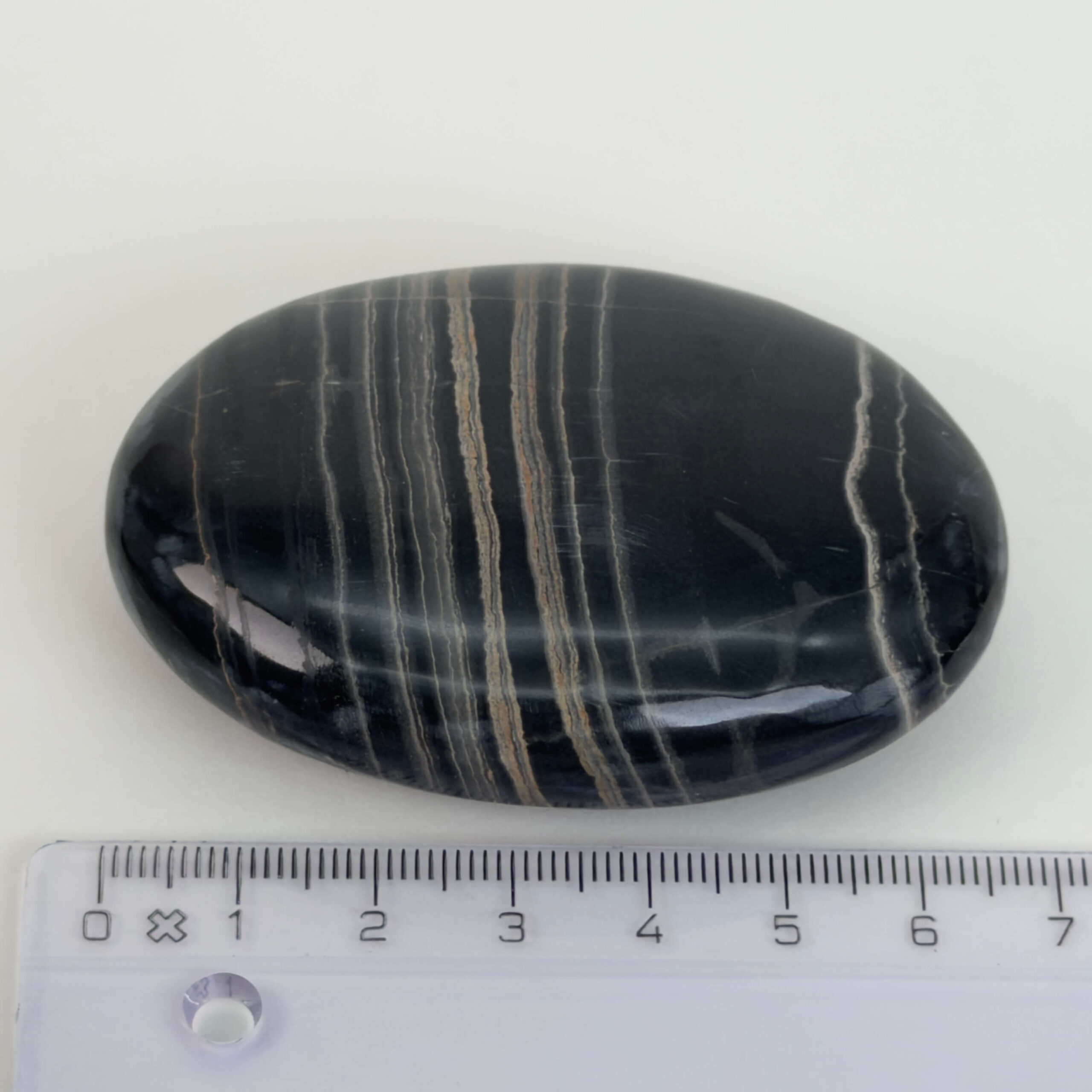 Sort Båndet Onyx Håndsten med glat, poleret overflade og naturlige sorte, grå og hvide bånd, der symboliserer grounding, beskyttelse og indre styrke.