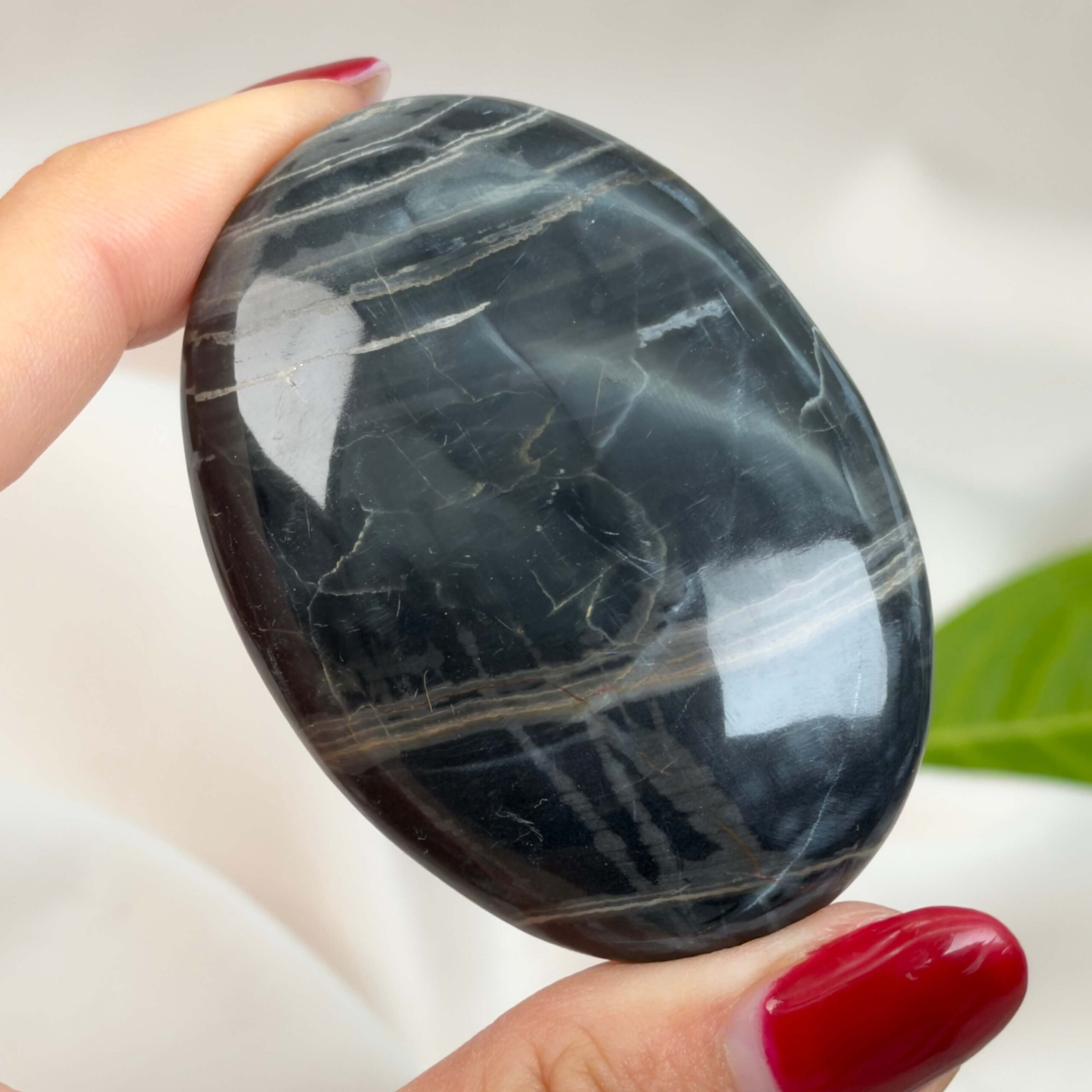 Sort Båndet Onyx Håndsten med glat, poleret overflade og naturlige sorte, grå og hvide bånd, der symboliserer grounding, beskyttelse og indre styrke.